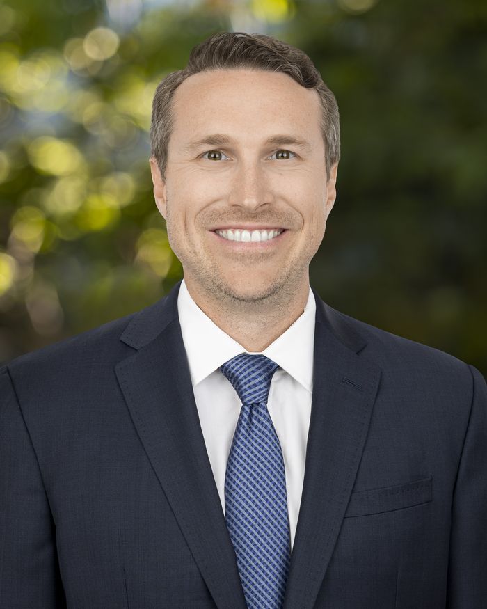 Garrett Hedstrom, Controller at Arroyo Capital, wearing a navy suit and blue tie against a blurred green background